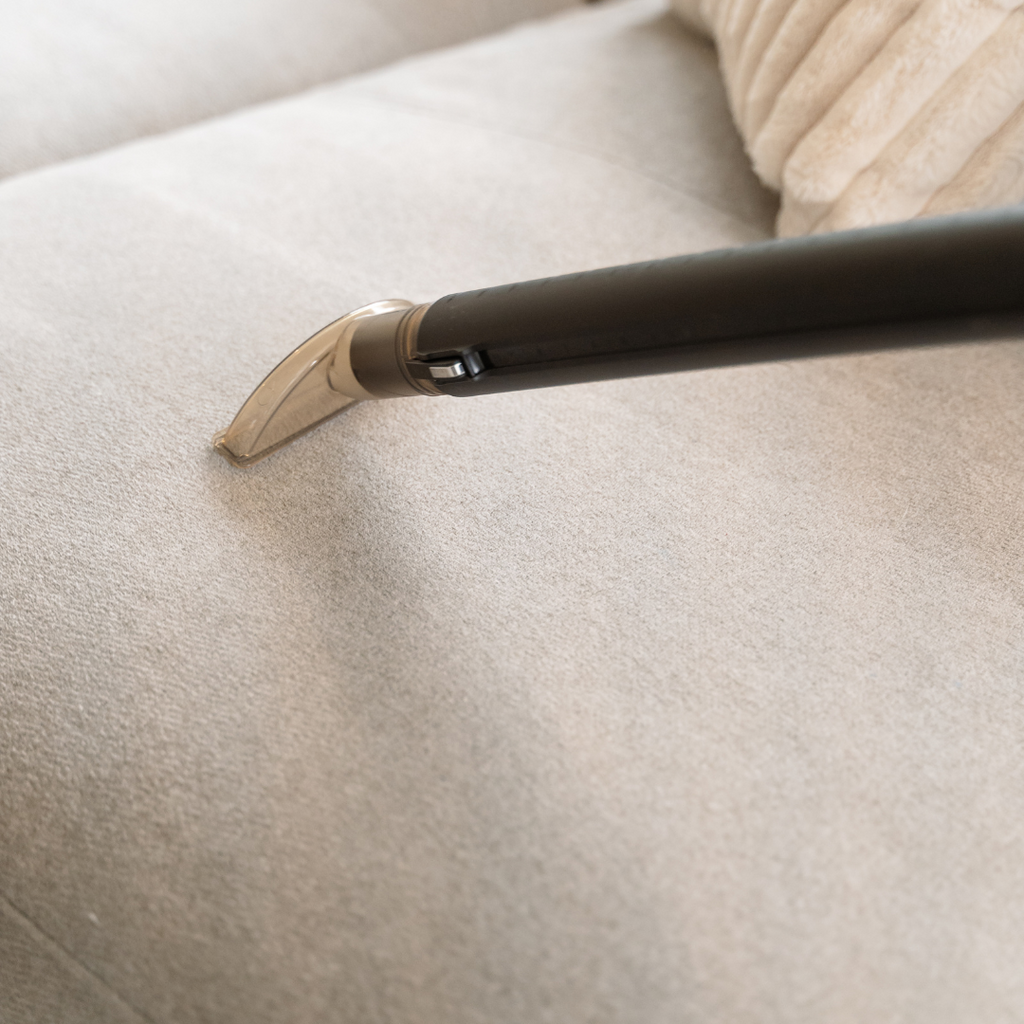 HYLA upholstery nozzle attached to a black hose handle cleaning a light beige couch cushion.